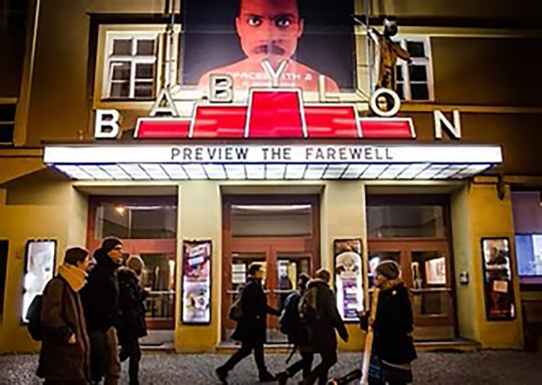 An exterior shot at nighttime of the classic Babylon Theater with people walking past. The marquee says Preview the Farewell.
