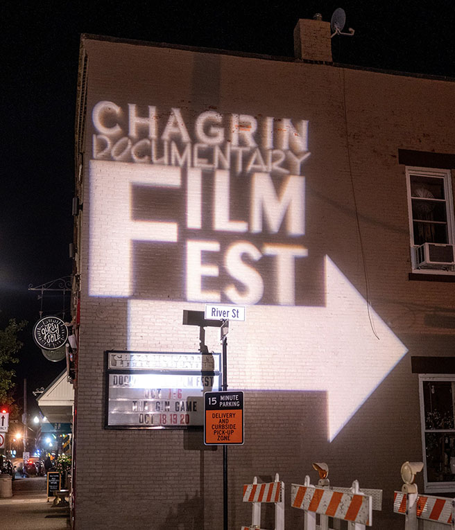 A brick wall of a building in Chagrin Falls at night with the festival name and a directional arrow cast upon the wall in white light.
