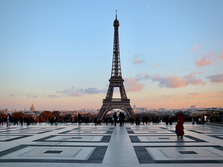 The Eiffel Tower and its plaza in the early morning, silhouettes of people on the plaza in the distance.