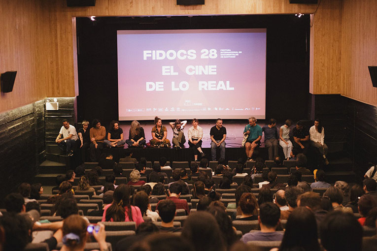 FIDOCs audience in a theater with a screen at the front that reads FIDOCS 28 El Cine De Lo Real in white block letters.