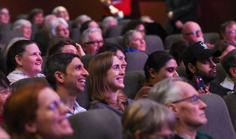 An audience in a theater listening to a speaker at the festival.