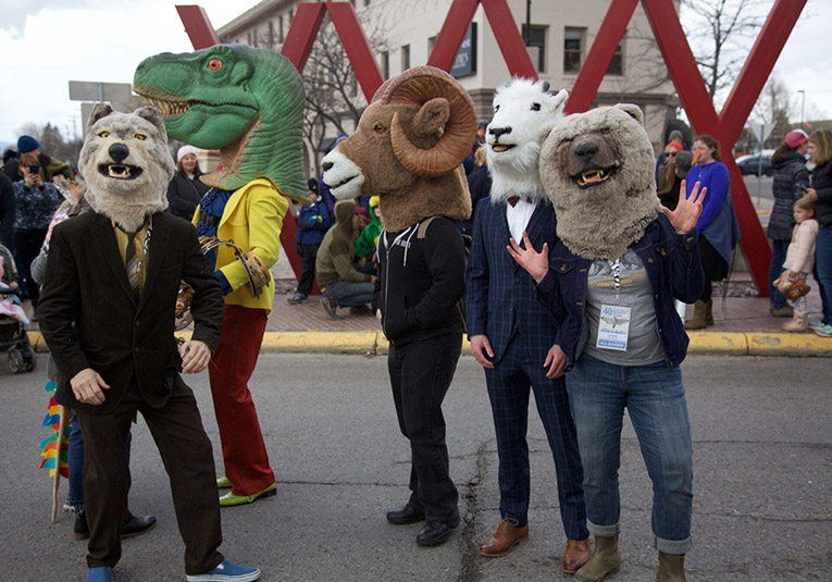 Festival goers in animal heads: a wolf, a tyrannosaurus, a bighorn sheep, a mountain goat, and a grizzly bear.