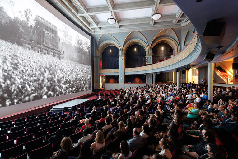 An audience in the American Museum of Natural History theater. The film still on the screen is from a documentary called "Seeds."