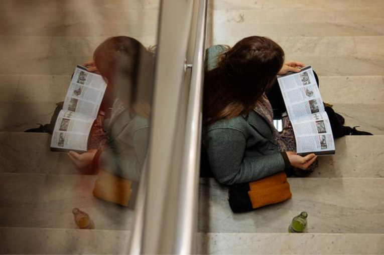 An image from above of a woman sitting on the floor looking at a program for the festival.