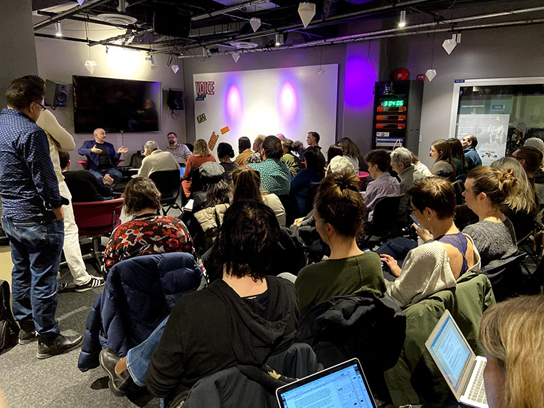 Interior conference room shot from behind the audience watching two people on the stage.