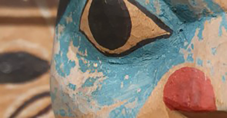 A close-up photo of the eye, nose, and cheek of a face on a totem pole in blue, white, and orange.