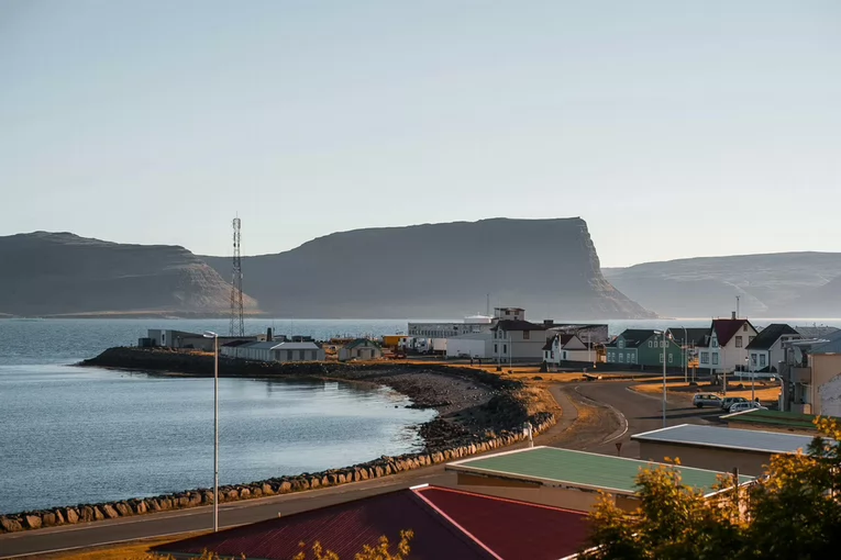 An exterior view of Skjaldborg, Iceland, with the ocean and a road in the foreground and rocky cliffs in the background.