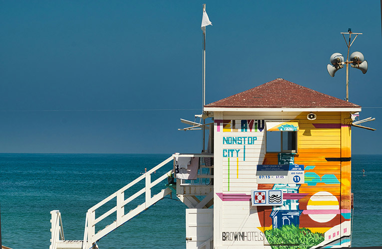 A lifeguard house on a sunny beach in Tel Aviv with a brightly colored mural and the words Tel Aviv Nonstop City in rainbow letters.