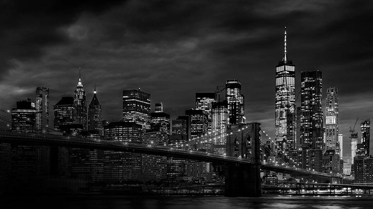 Night skyline of lower Manhattan with the Brooklyn Bridge in the foreground.